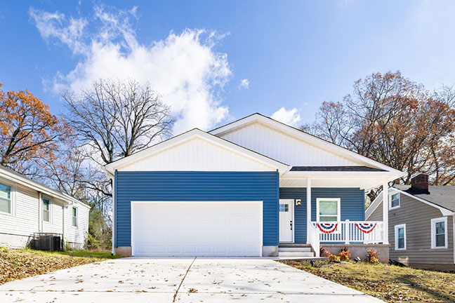 A manufactured home with blue siding and a driveway scattered with leaves