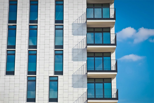 Four stories of a white-exterior apartment building with balconies on each level.