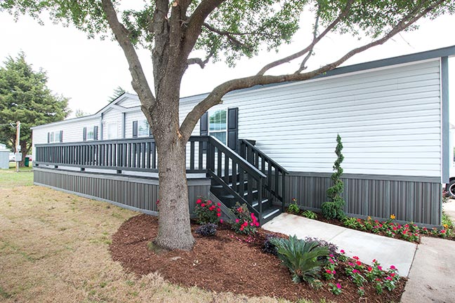A used mobile home with an extended porch and planted garden.