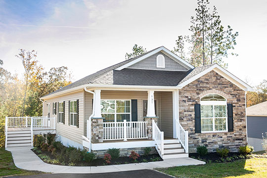 A mid-sized modern home pictured in the daytime. The house has white columns on its porch, beige vinyl siding, and gray shingles. In the current housing market, a home like this is much more expensive than it was five years ago. 