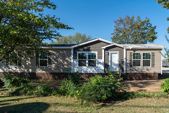  A manufactured home with beige vinyl siding partially shaded by a nearby tree. In a hot housing market, manufactured homes can be an affordable alternative to stick-built houses.