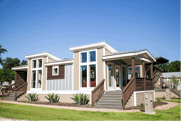  The exterior of a new manufactured home designed with a farmhouse look. The home includes plenty of natural wood features and large windows with thick white trim. Two beautiful covered porches stand on either side of the manufactured home.