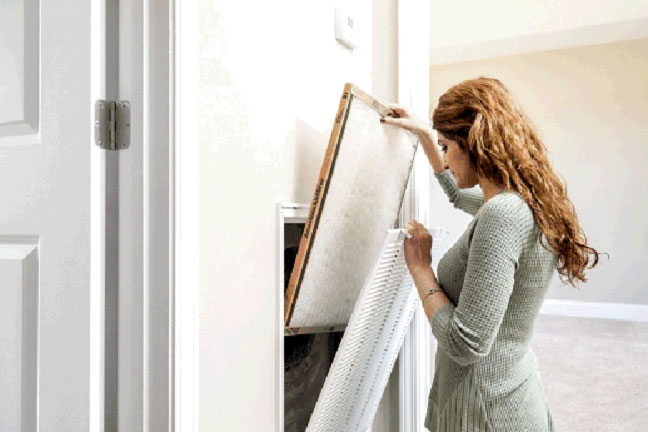 A woman changing out the filter inside her HVAC intake vent.