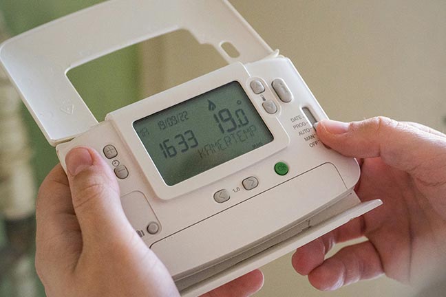 A person making adjustments to their thermostat.