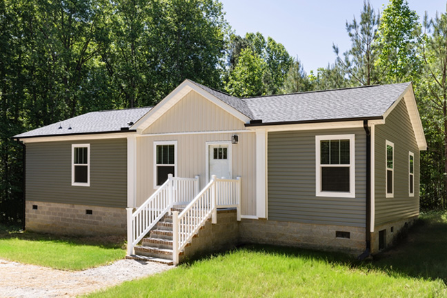 A manufactured home with dark grey siding and an entry with stone steps