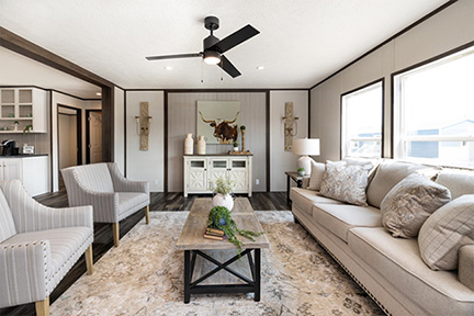 Cozy sun-lit living room with a black ceiling fan hanging over a gray coffee table.