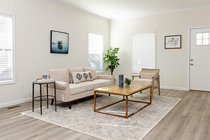 Sunlight shines into a minimally decorated living room with cream walls and gray flooring.