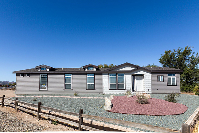 Mobile home with gray siding and a rock front yard surrounded by a wooden fence.