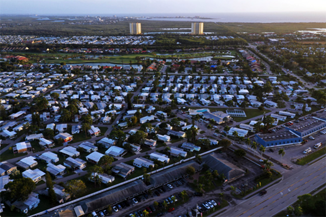 An aerial view of the sun rising over a large mobile home park near the ocean.