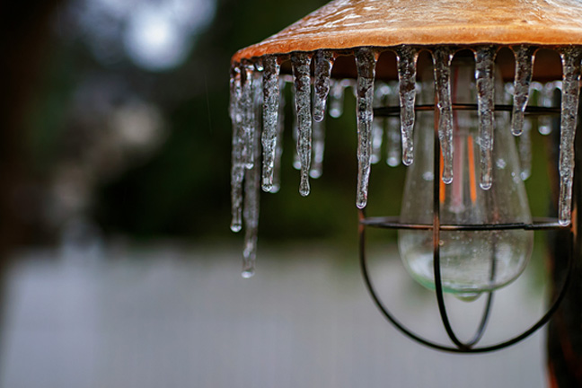 Icicles hang from an outside light, ice coating the top of it.