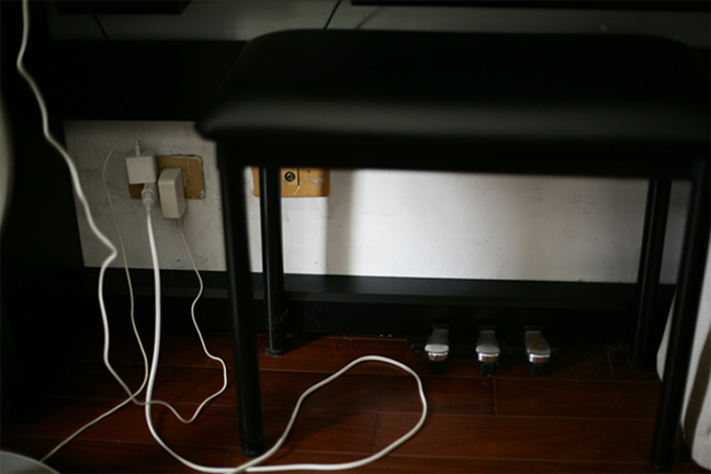 Numerous cords extend from an outlet beneath a piano, putting strain on the wiring.