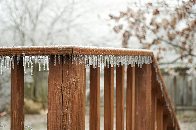 Icicles running along snow-topped deck railing.