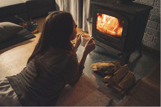 Woman keeping warm in her home relaxing in front of a small wood stove 